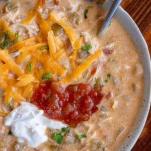 bowl of chicken taco soup topped with sour cream, salsa, shredded cheese, and fresh herbs