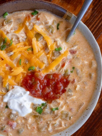 bowl of chicken taco soup topped with sour cream, salsa, shredded cheese, and fresh herbs