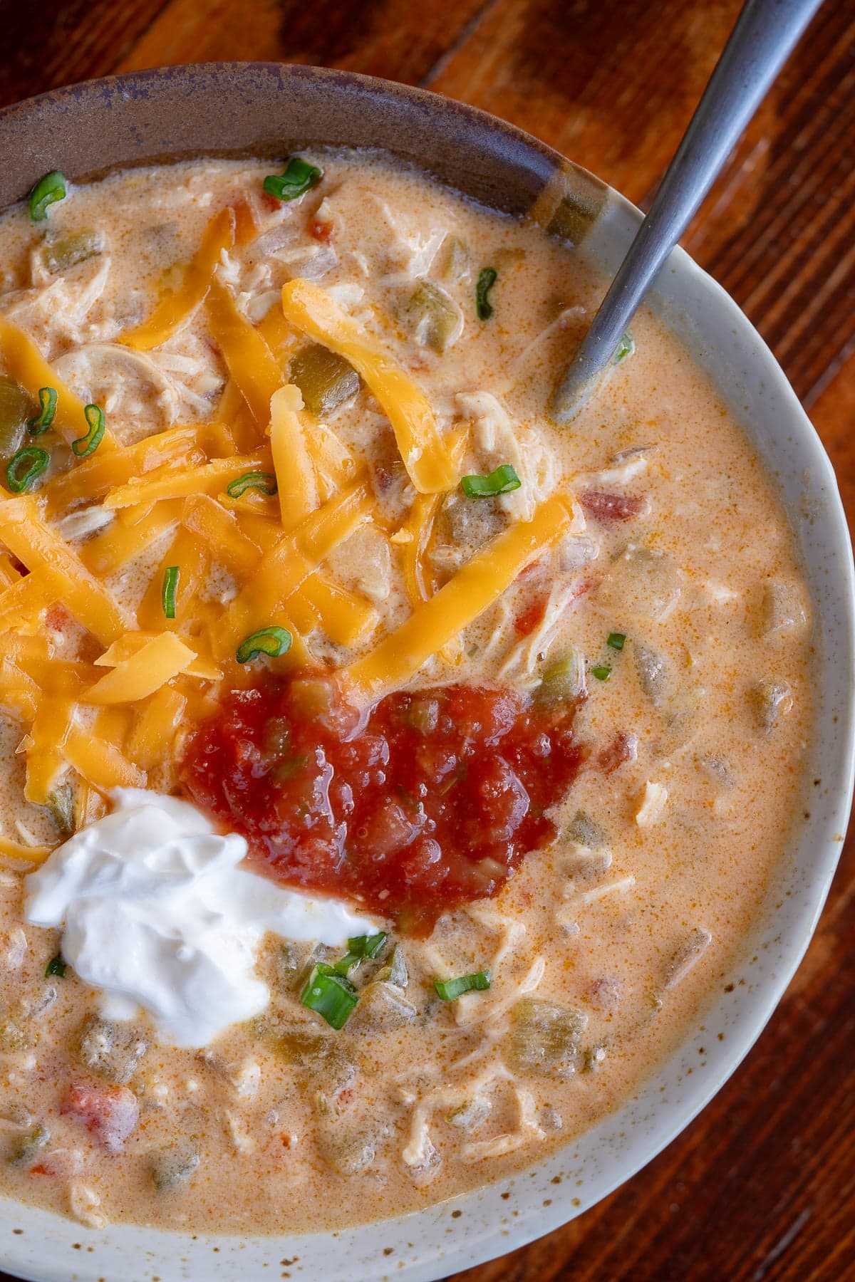 bowl of chicken taco soup topped with sour cream, salsa, shredded cheese, and fresh herbs