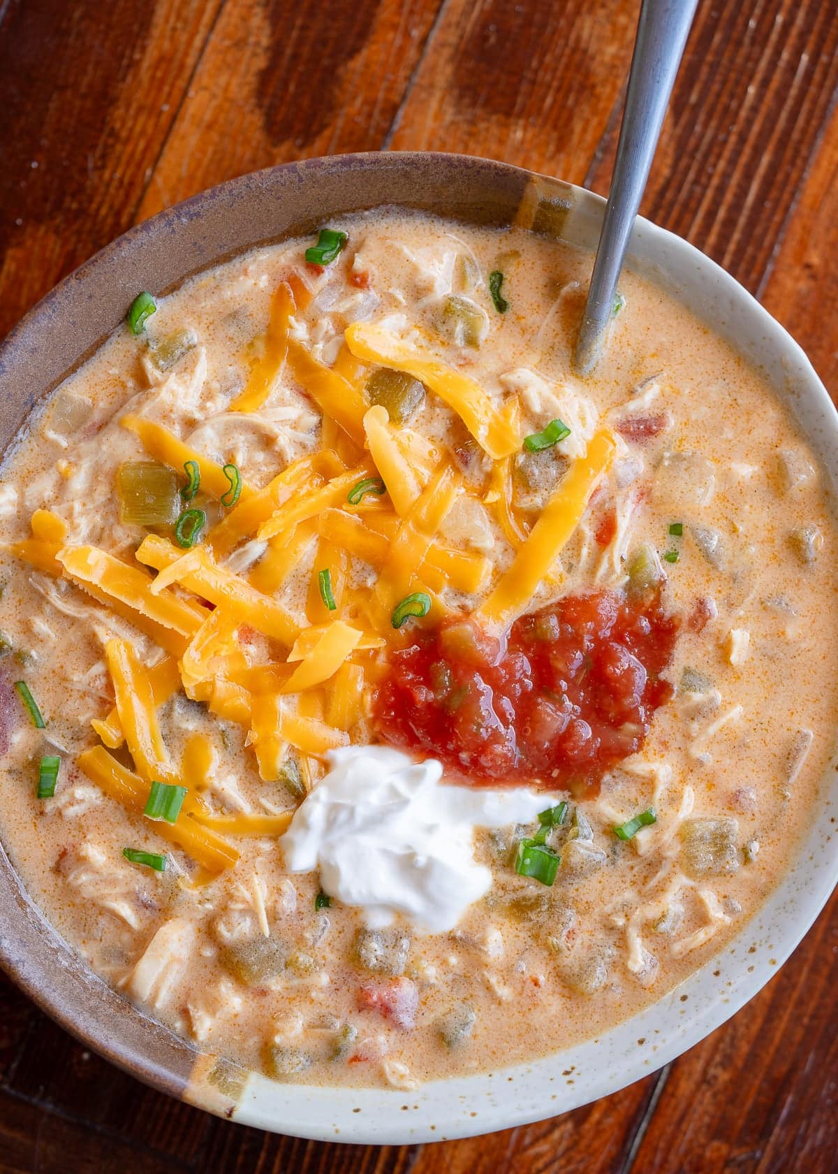 a bowl full of creamy chicken taco soup topped with cheddar, salsa, sour cream, and green onions