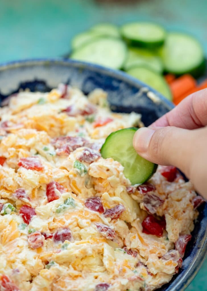 a hand dipping a cucumber into the best pimento cheese dip ever