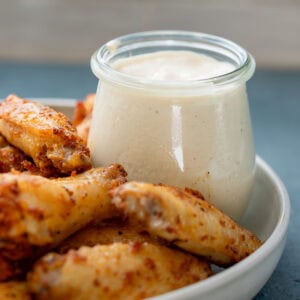 a jar of alabama white sauce on a platter with dry rub wings