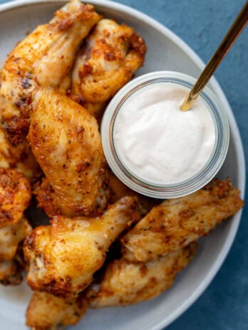 overhead shot showing ultra creamy alabama white sauce in a jar on a plate with dry rub wings