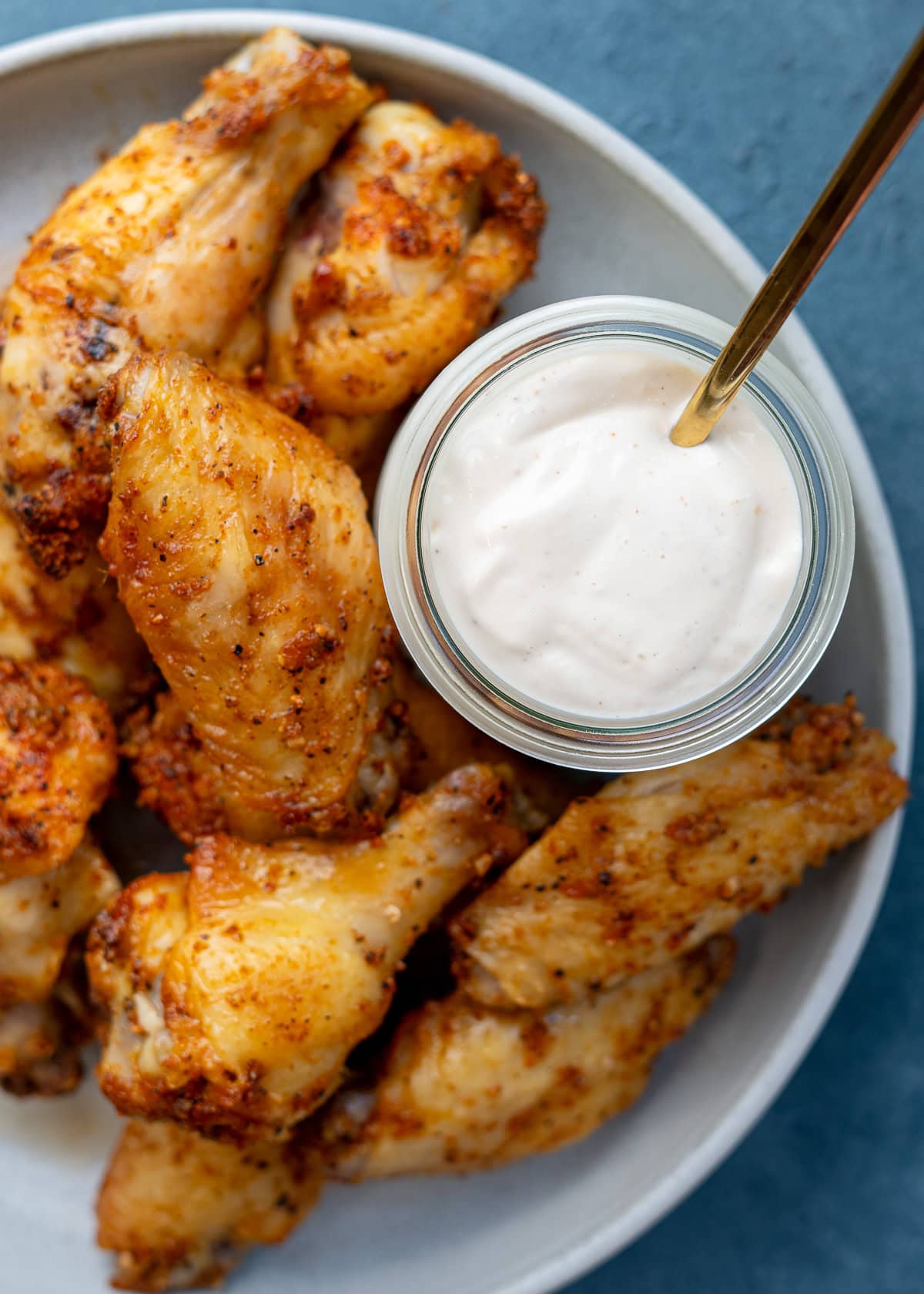 overhead shot showing ultra creamy alabama white sauce in a jar on a plate with dry rub wings