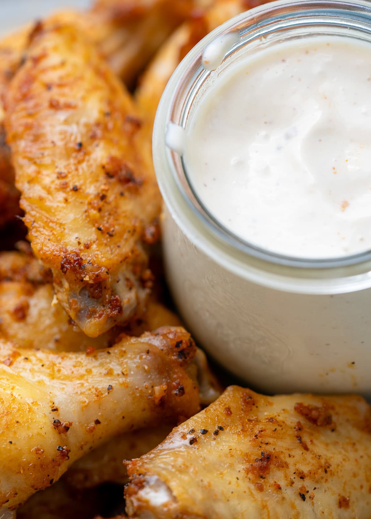 closeup of creamy copycat newks white bbq sauce beside a pile of chicken wings