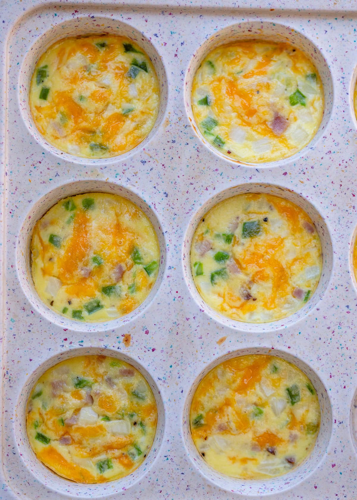 egg, ham, cheese, peppers, and onion  in the wells of a silicone muffin pan
