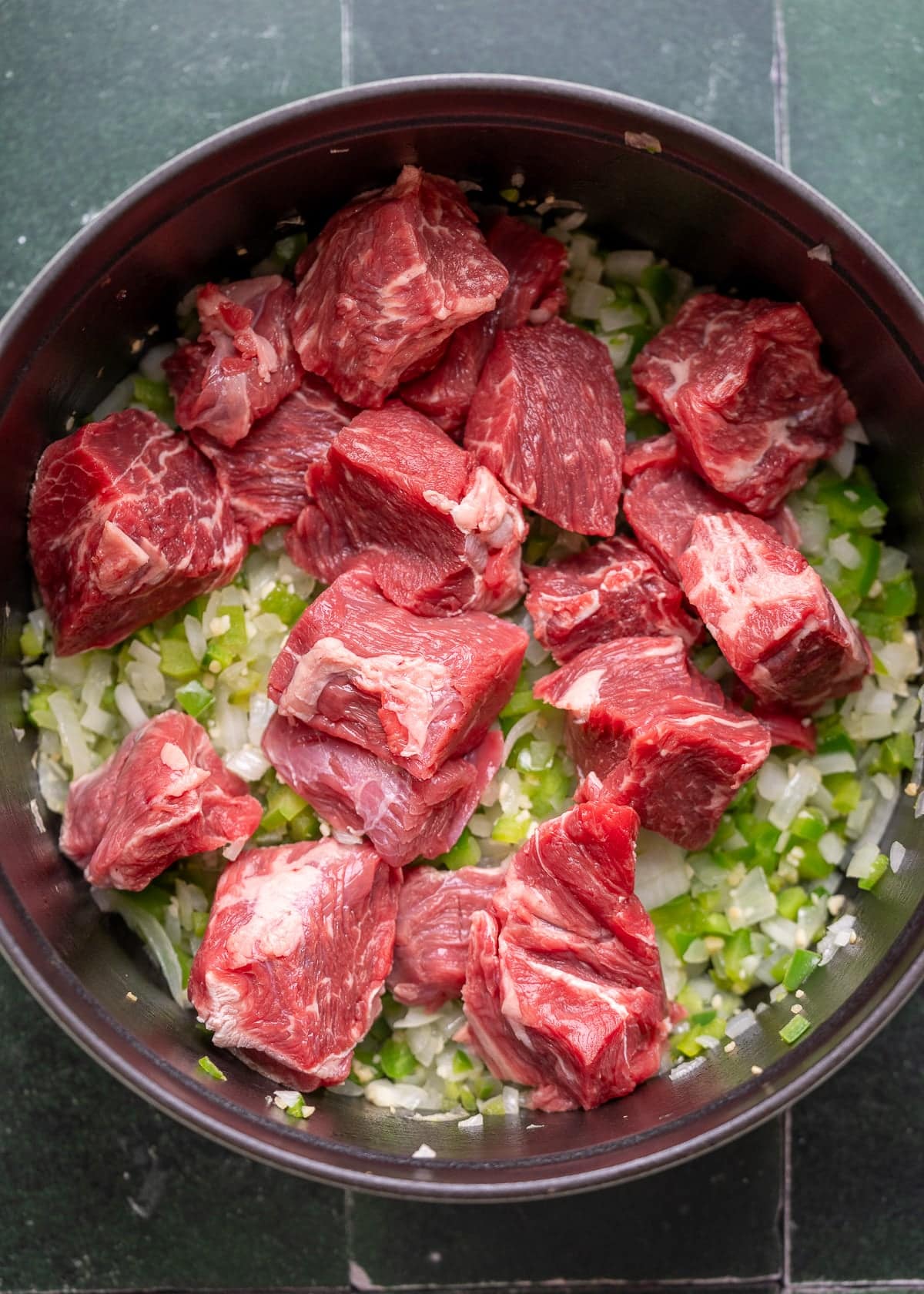 sauteed onion, bell pepper, jalapeno, and garlic in a pot with chunks of beef chuck roast