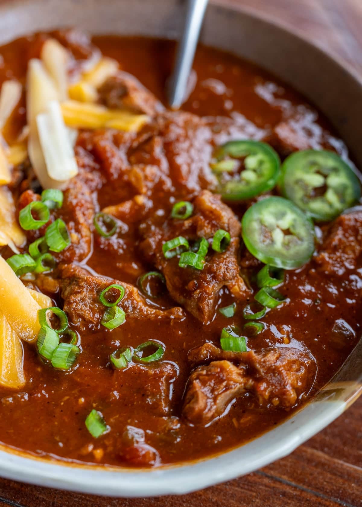 the best chili con carne recipe in a bowl topped with green onions, jalapenos, and cheese