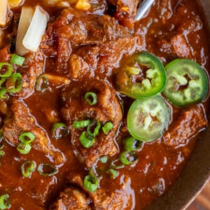 closeup of rich, thick chili con carne topped with green onions, jalapenos, and shredded cheese