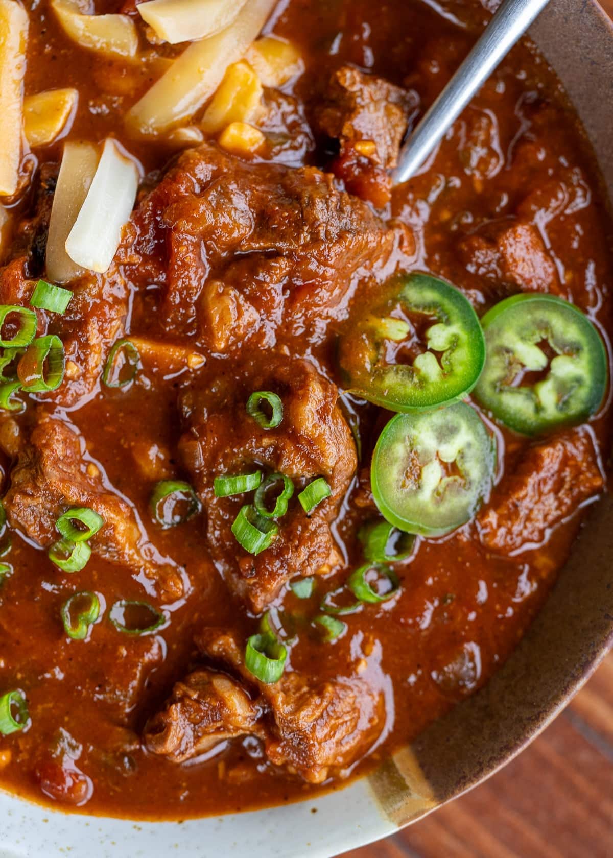 closeup of rich, thick chili con carne topped with green onions, jalapenos, and shredded cheese